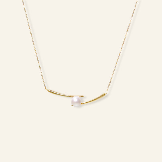 Gold necklace with a single pearl on a white background