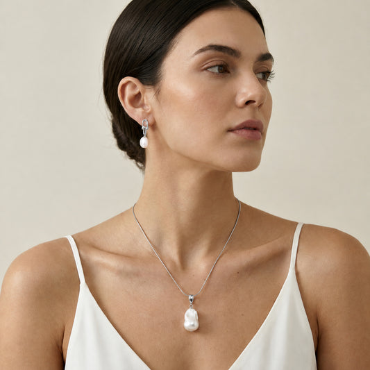 Model wearing a gold necklace with a large white baroque freshwater pearl pendant resting at the centre of the neckline.