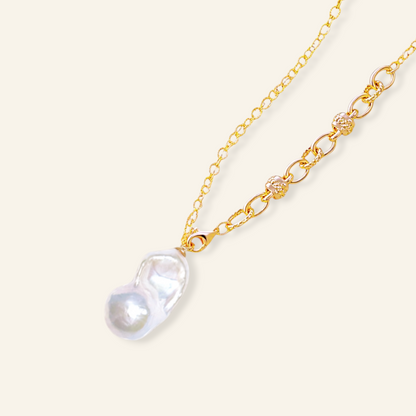 A gold chain necklace featuring a large, irregular white baroque pearl pendant 