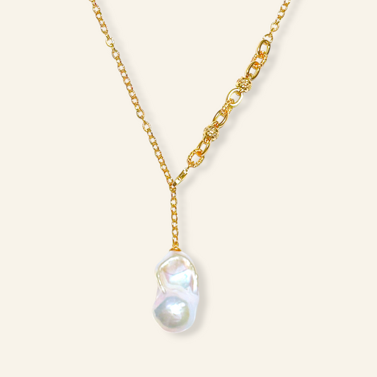 A gold Y-necklace featuring a large, irregular baroque pearl pendant 