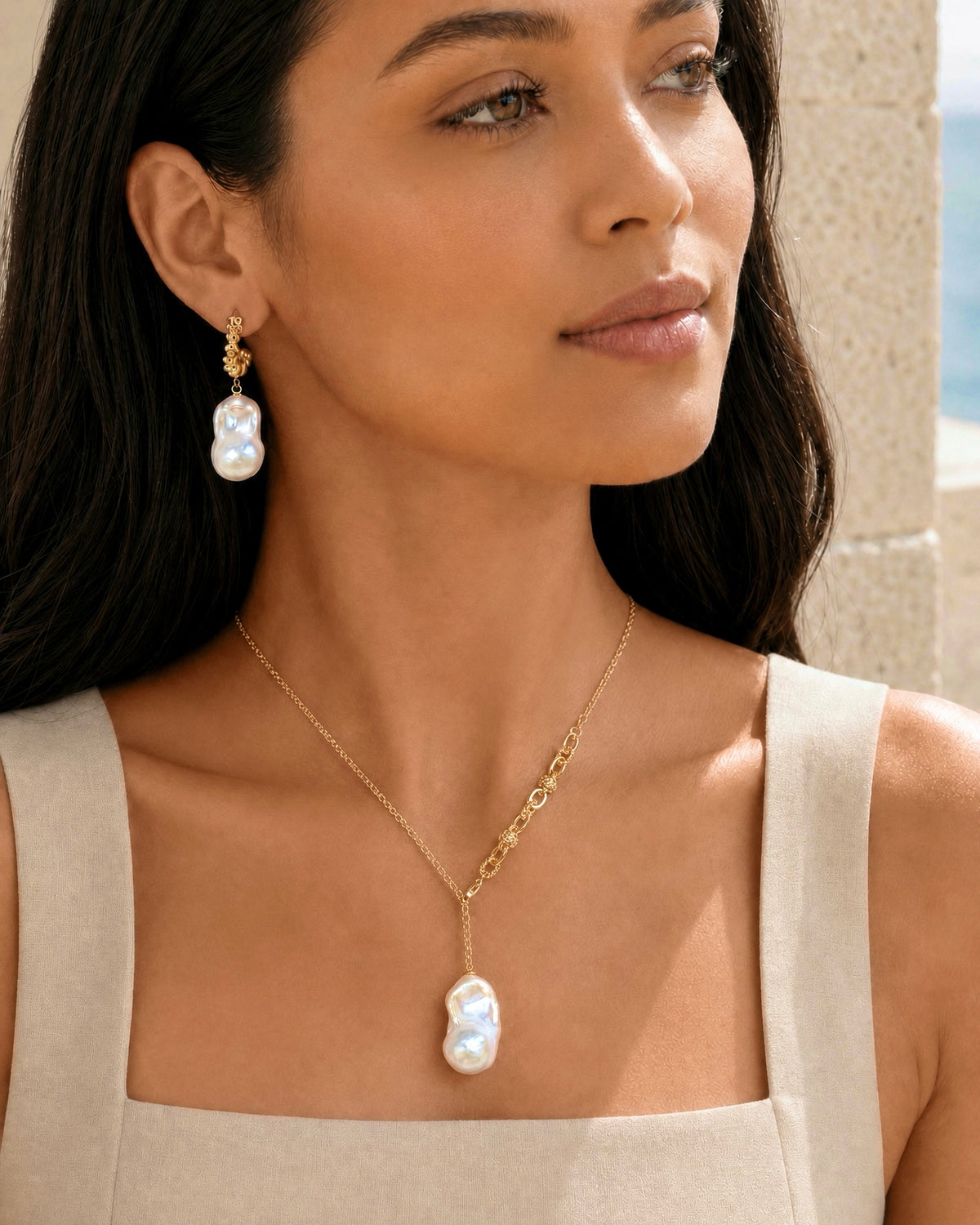 A woman wearing a gold necklace with a large baroque pearl pendant and matching drop earrings