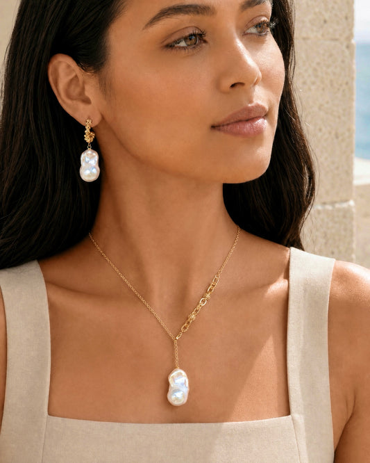 A woman wearing a gold necklace with a large baroque pearl pendant and matching drop earrings