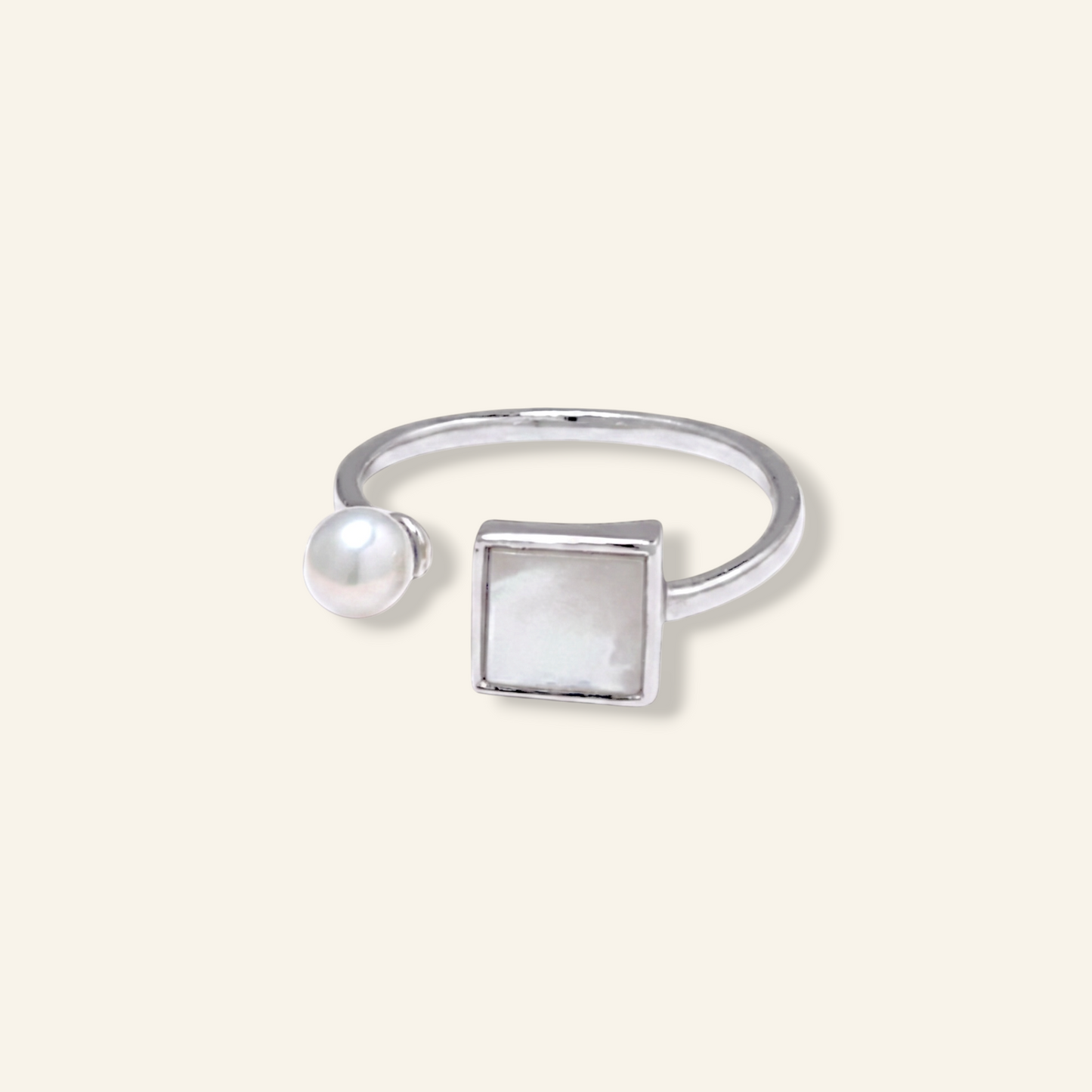 Silver ring with a pearl and square stone on a light beige background