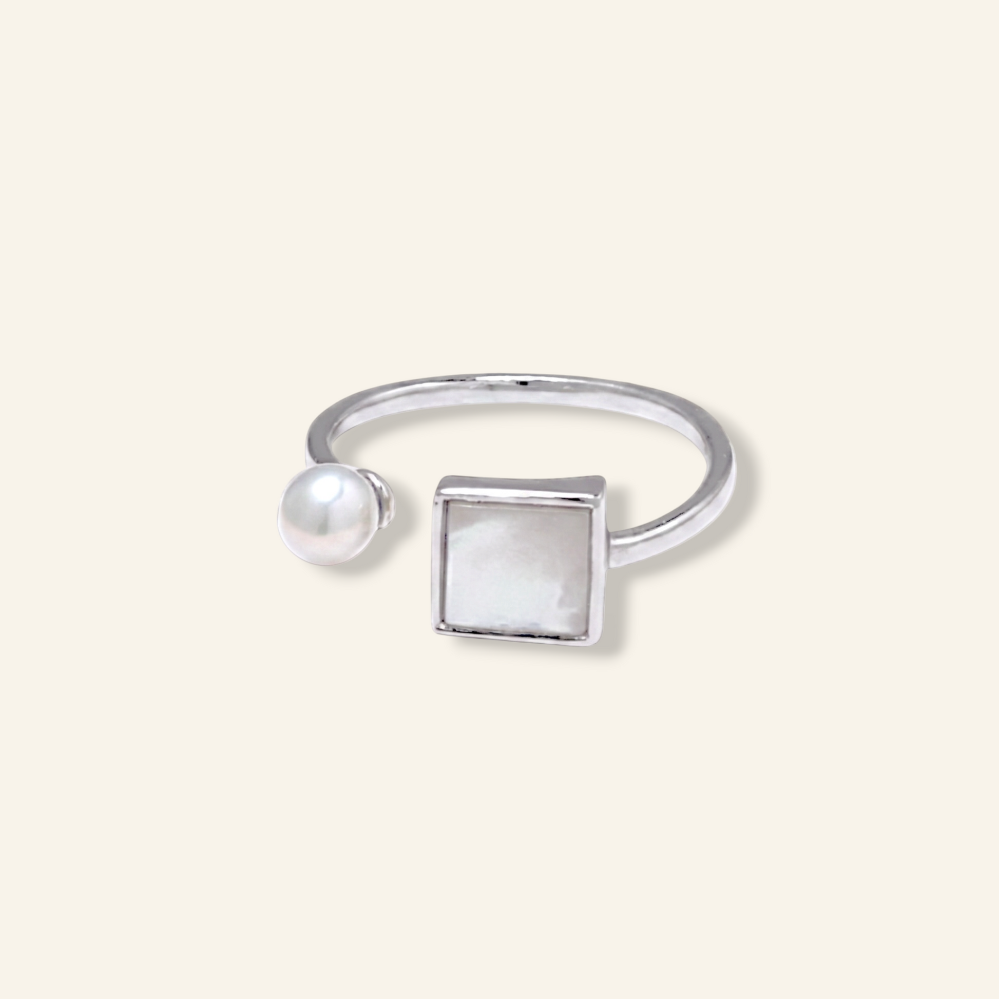 Silver ring with a pearl and square stone on a light beige background