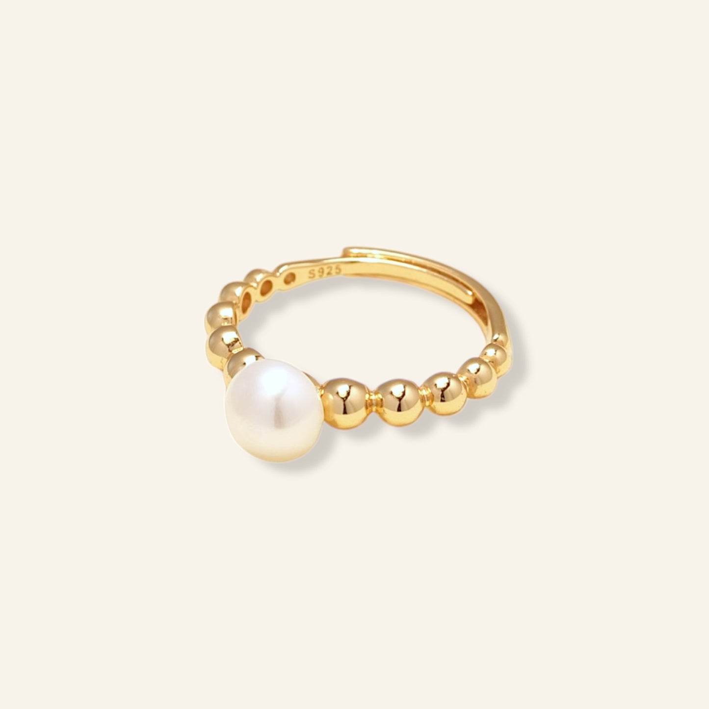 Gold ring with a pearl on a light beige background