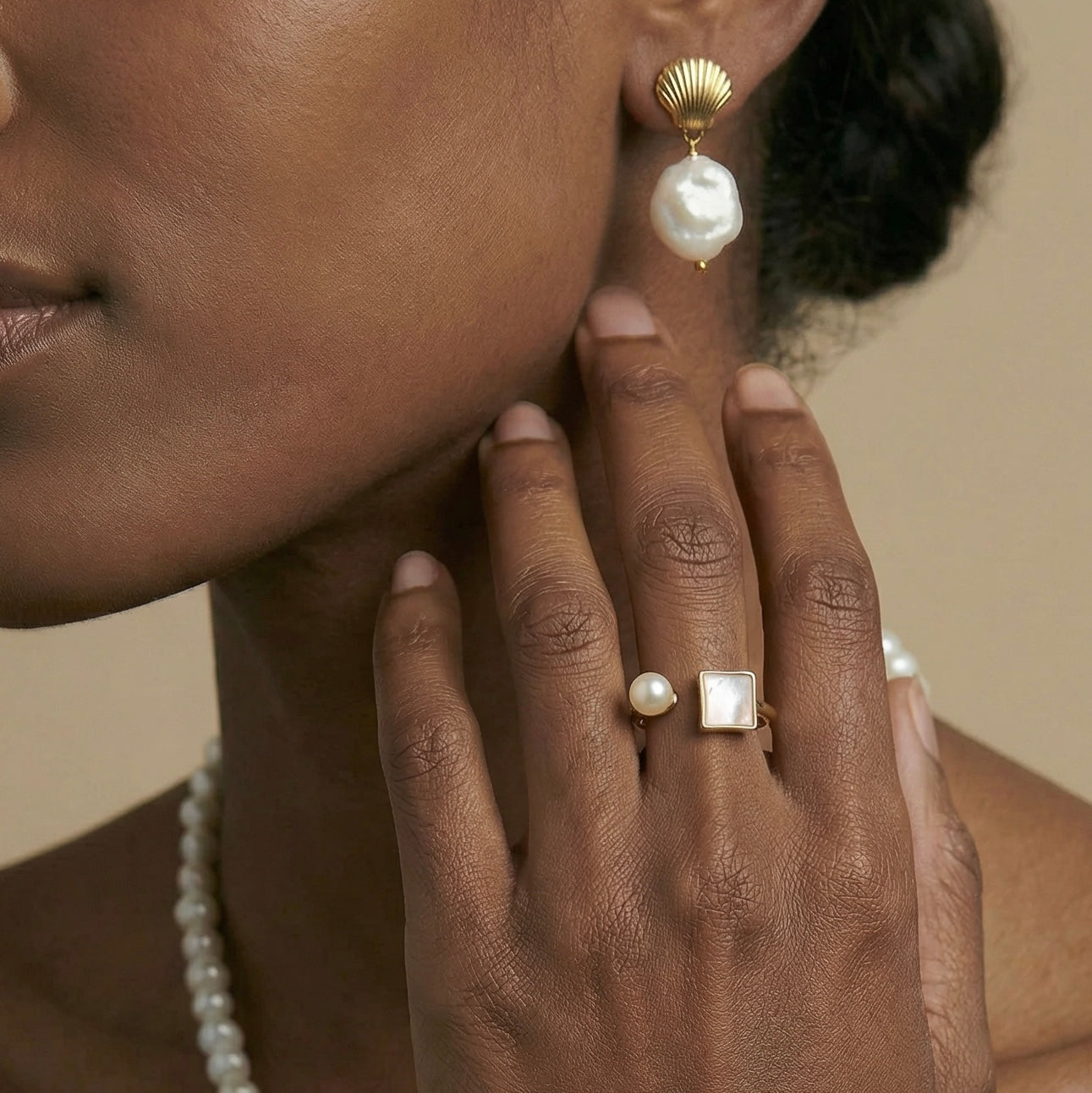 Close-up of a woman wearing gold earrings and a ring with pearls