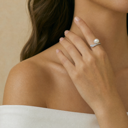 Close-up of a hand wearing a silver ring with a pearl on a neutral background
