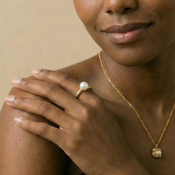 Woman wearing a gold necklace and ring with a pearl 