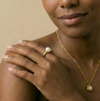 Woman wearing a gold necklace and ring with a pearl 