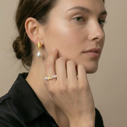 Woman wearing gold earrings and a ring with a pearl