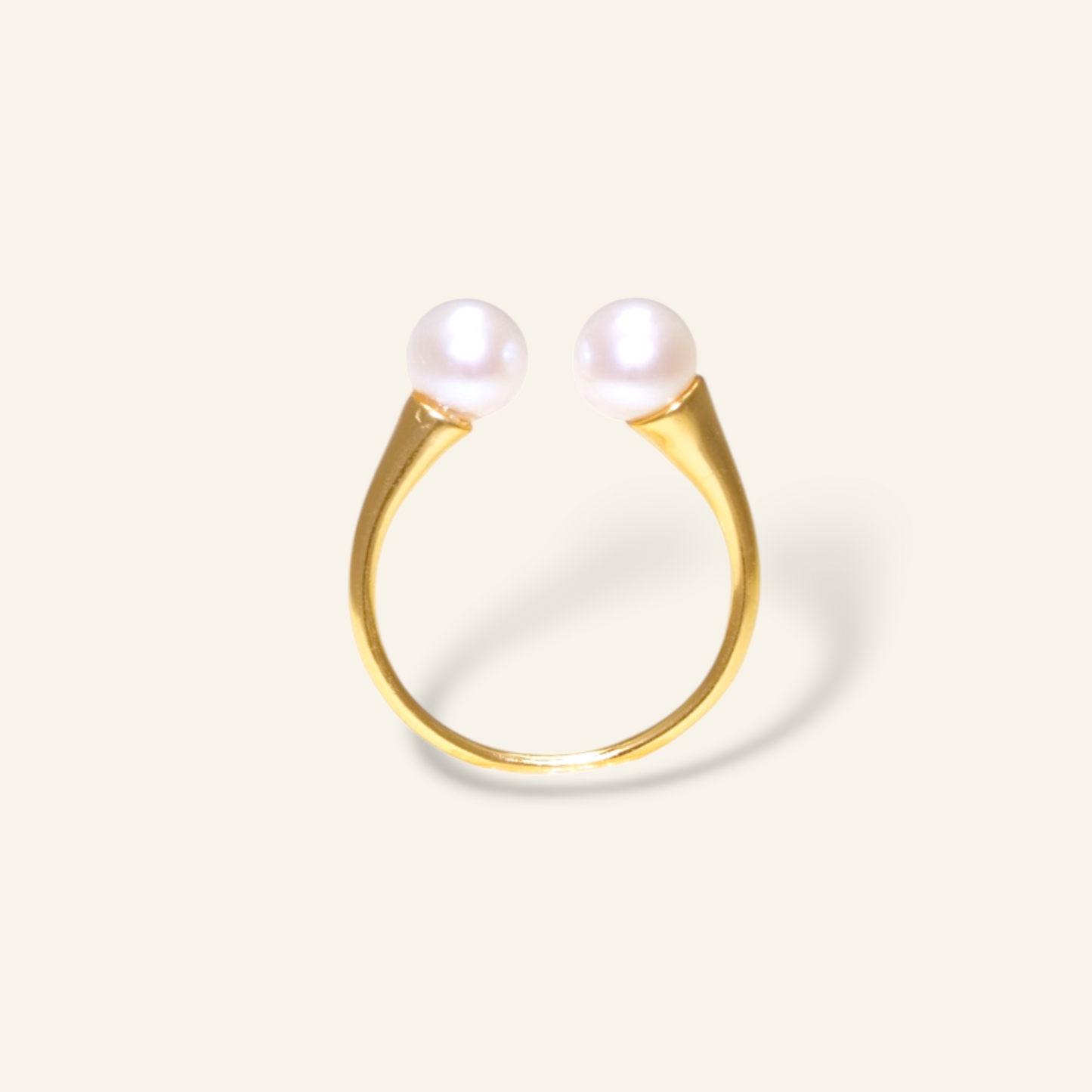 Gold ring with two pearls on a light beige background