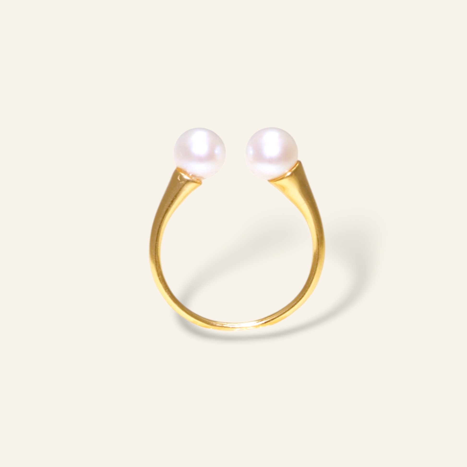 Gold ring with two pearls on a light beige background