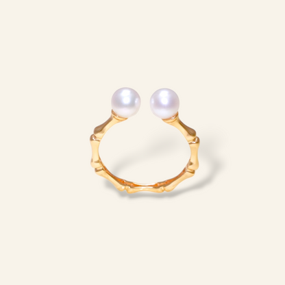 Gold ring with two pearls on a light beige background